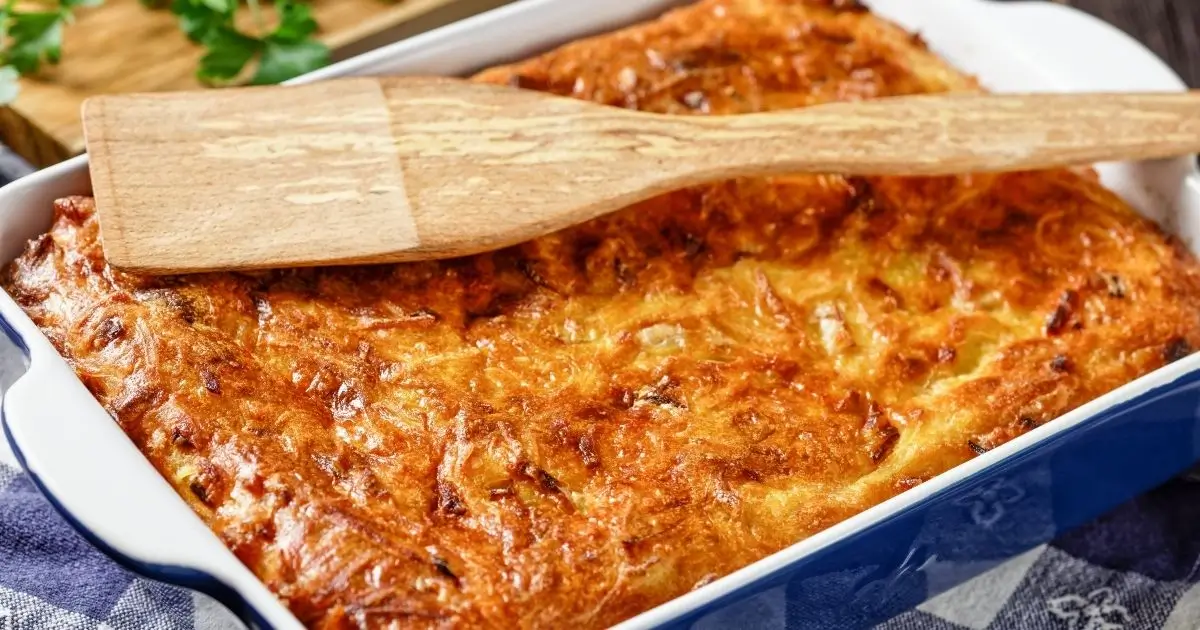 Golden-brown baked chicken dressing in a casserole dish with a wooden spatula resting on top.